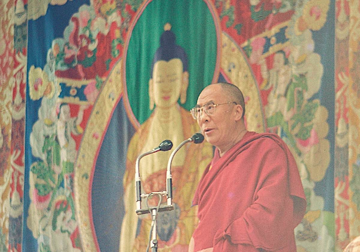 The Dalai Lama at a public speaking engagment stands in front of one of the appliqué thangkas of Shakyamuni Buddha.